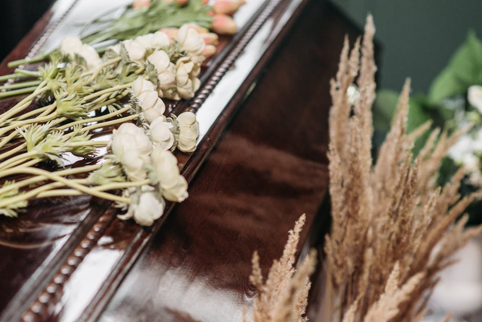 A close-up view of a floral arrangement featuring white roses and pale pink tulips, laid out on a polished wooden surface, with some stems extending outward. The flowers are arranged in a linear bouqu